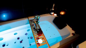 A bathtub with rose petals, a bottle of champagne, and a candle.