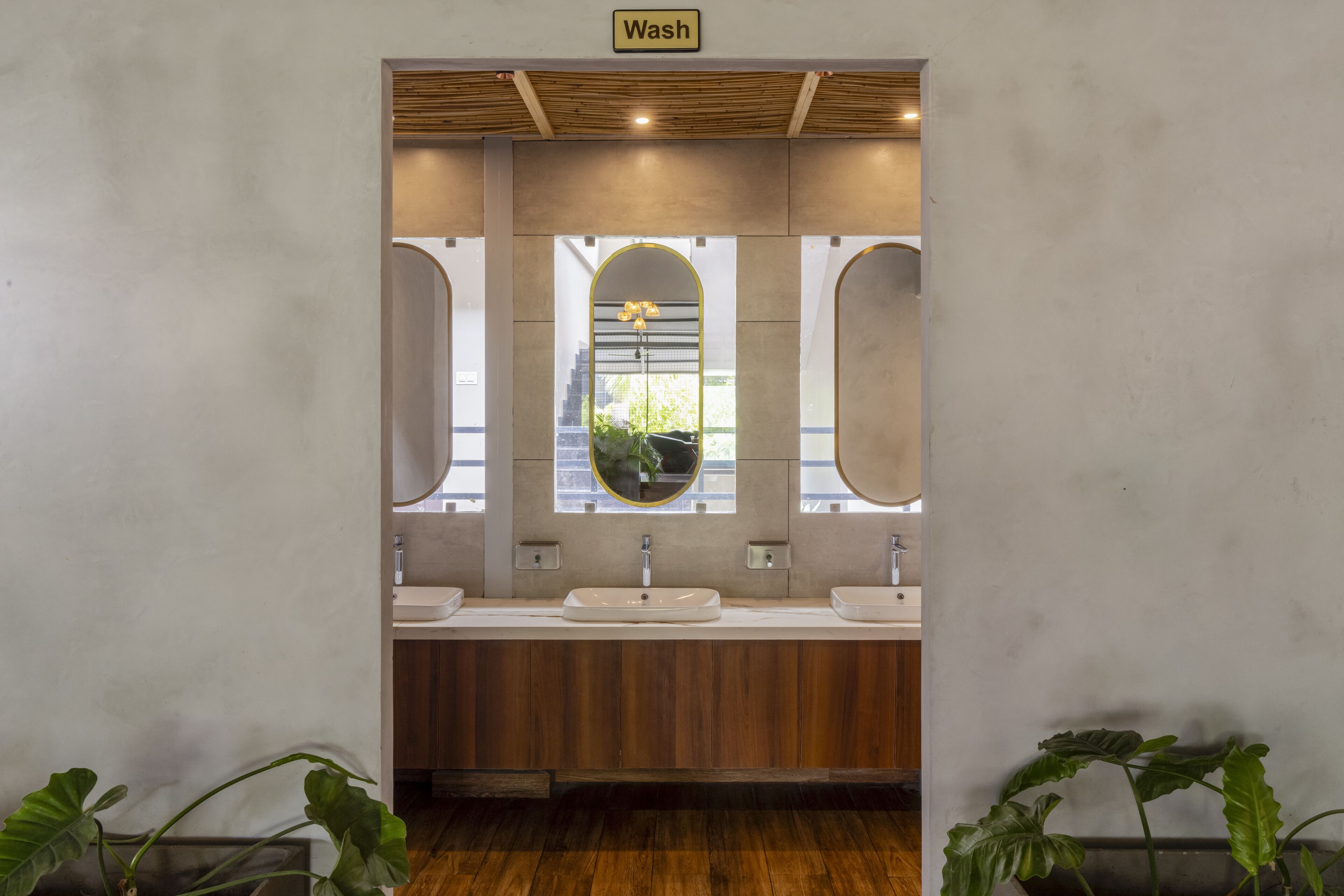 A modern bathroom with three sinks, a wooden vanity, and a mirror with a circular frame.