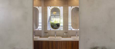 A modern bathroom with three sinks, a wooden vanity, and a mirror with a circular frame.