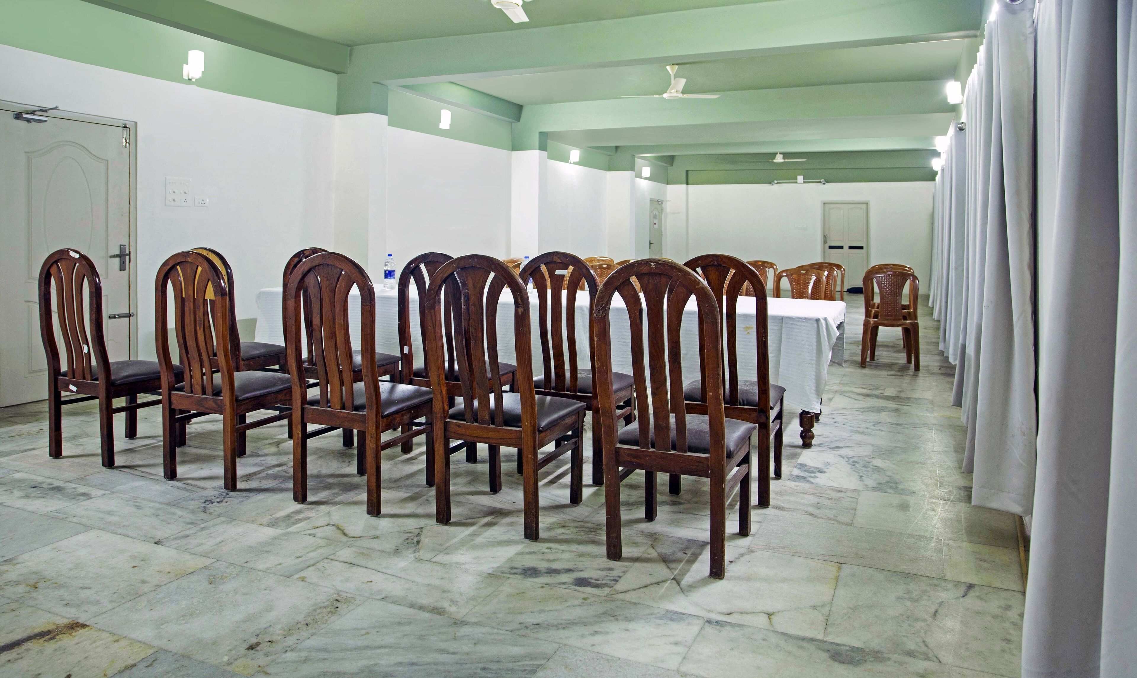 Una habitación con filas de sillas y mesas de madera, suelo de baldosas y techo verde.