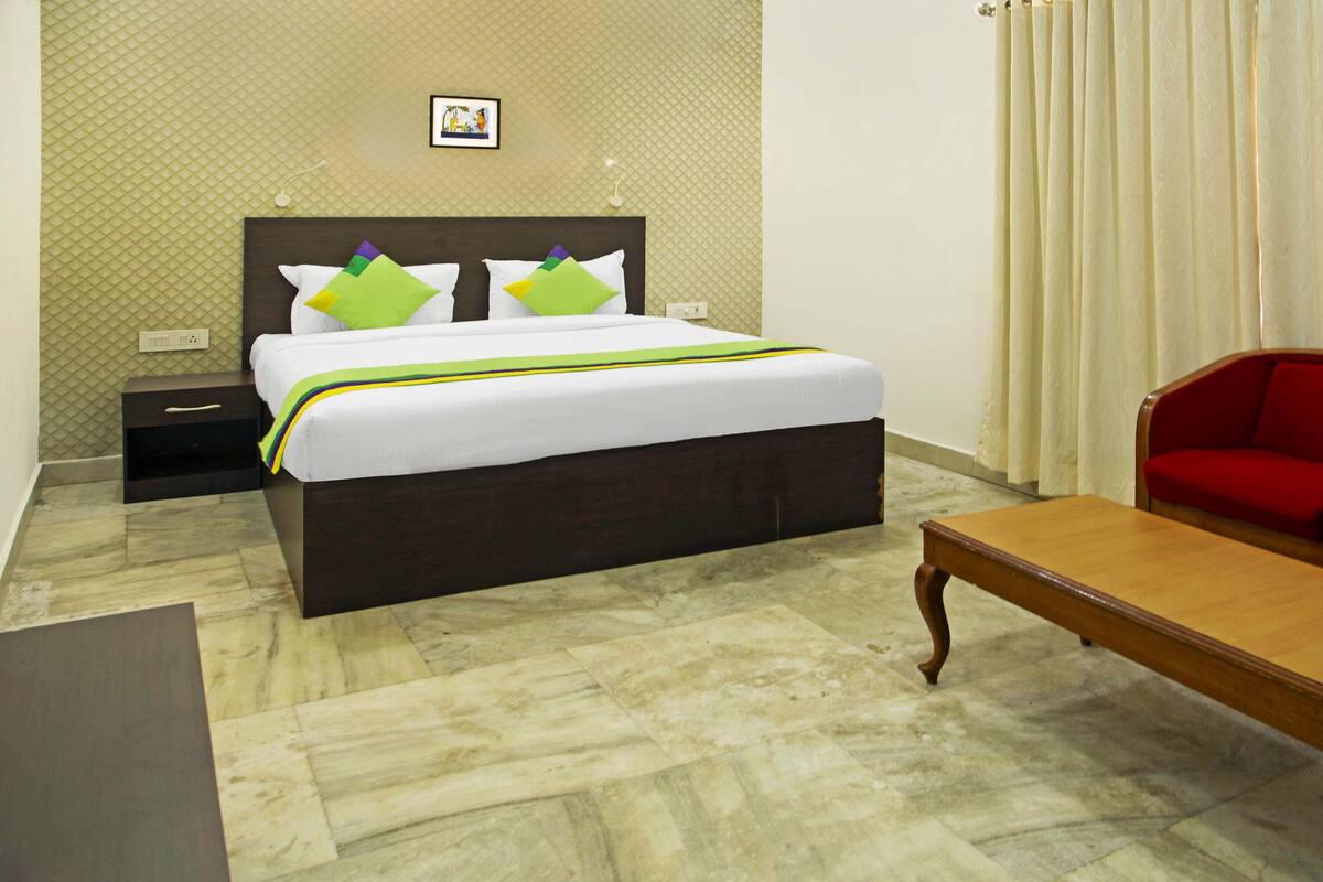 Una habitación de hotel con cama, mesita de noche, sillón rojo y mesa de madera.