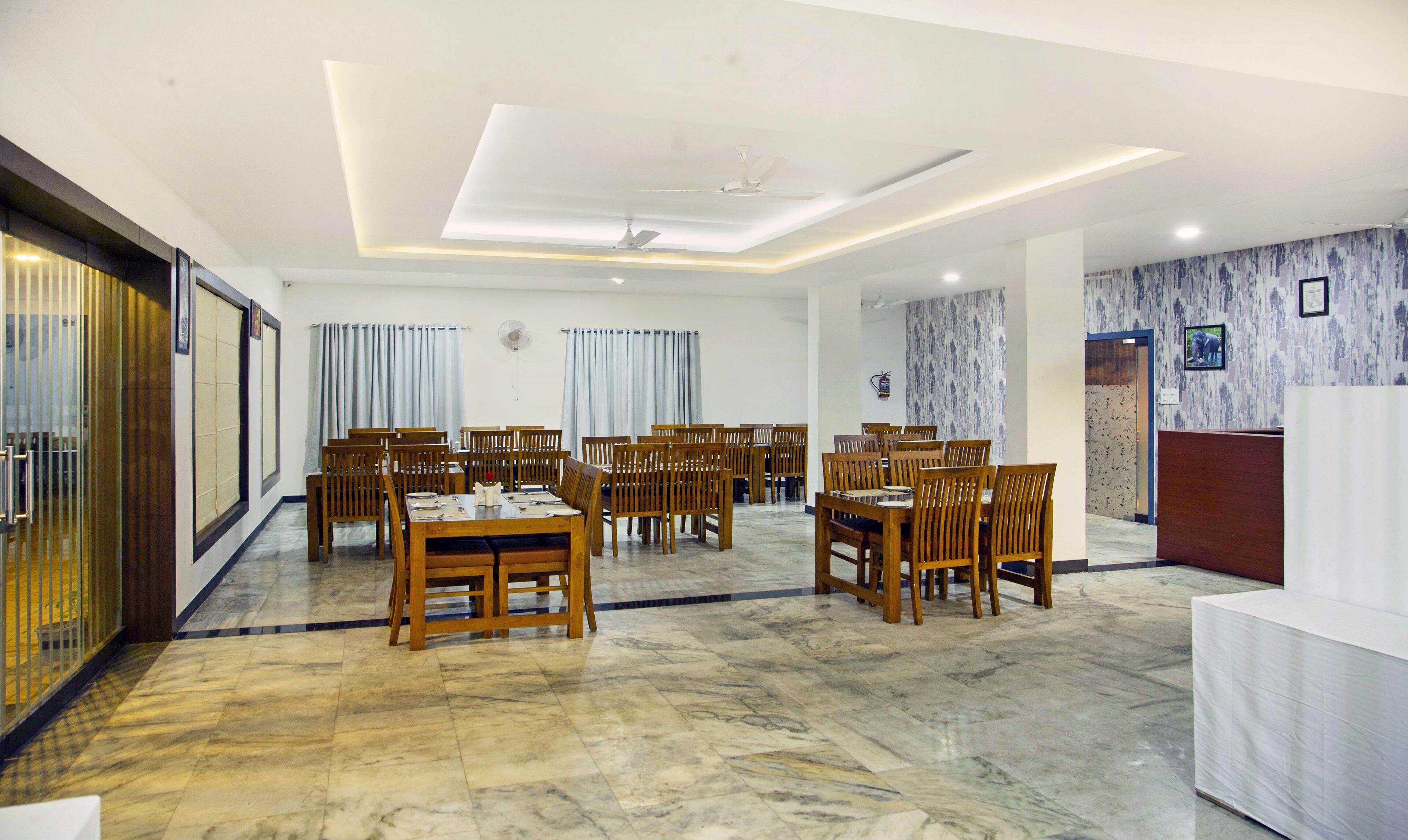 A spacious dining area with wooden tables and chairs, a ceiling fan, and a reception desk.