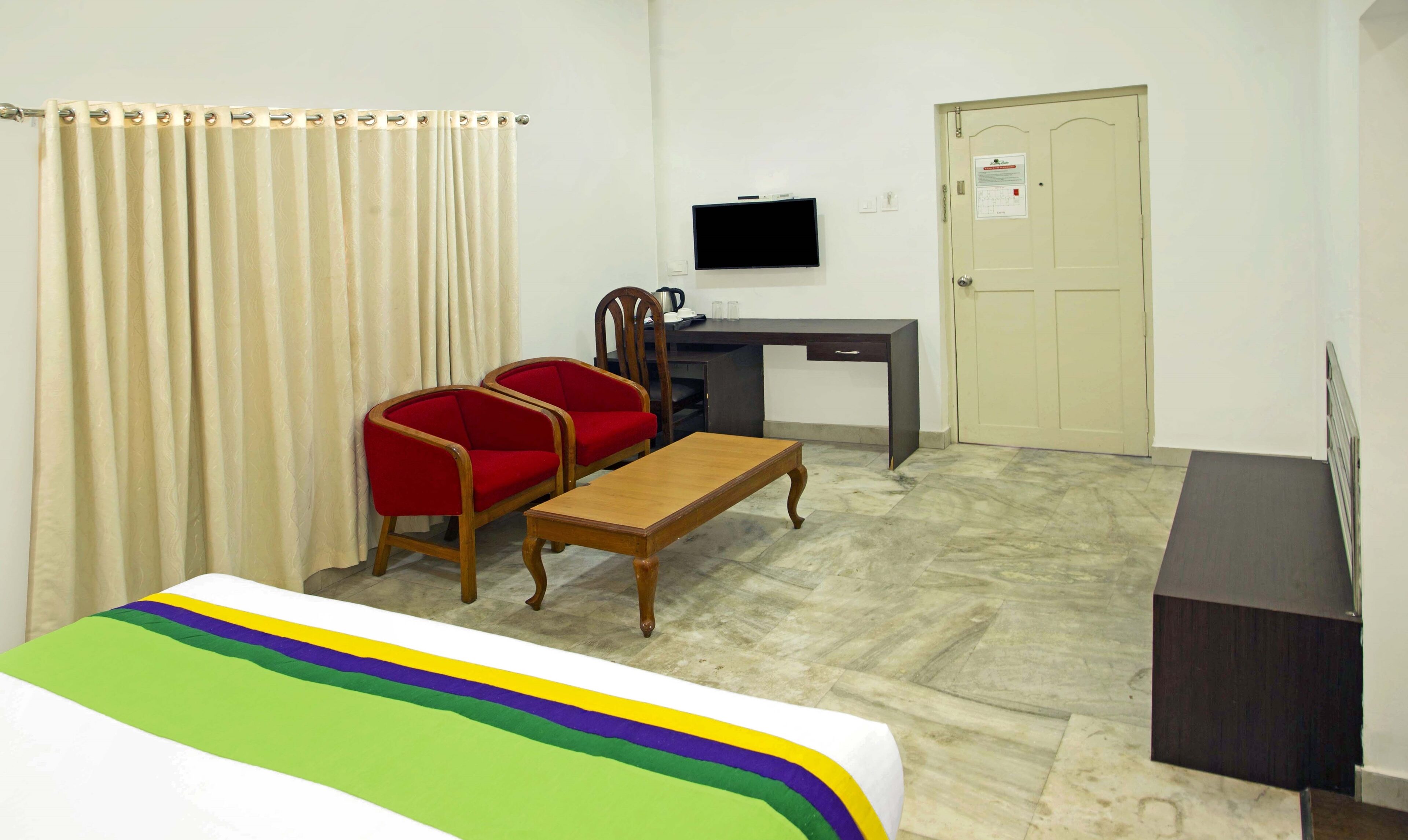 A room with a bed, a desk, a chair, a television, and a door.