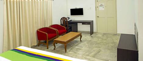 A room with a bed, a desk, a chair, a television, and a door.