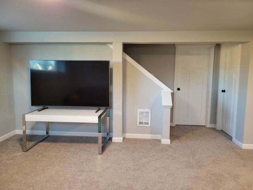 Een kamer met een flatscreen televisie op een standaard, een vloerbedekking, een trap en een deur.
