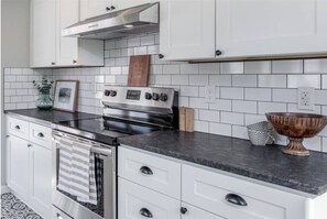 Una cocina con armarios blancos, una estufa de acero inoxidable y una encimera negra.