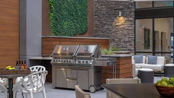 Un patio al aire libre con una parrilla de acero inoxidable, mobiliario de mimbre y una pared de piedra con vegetación.