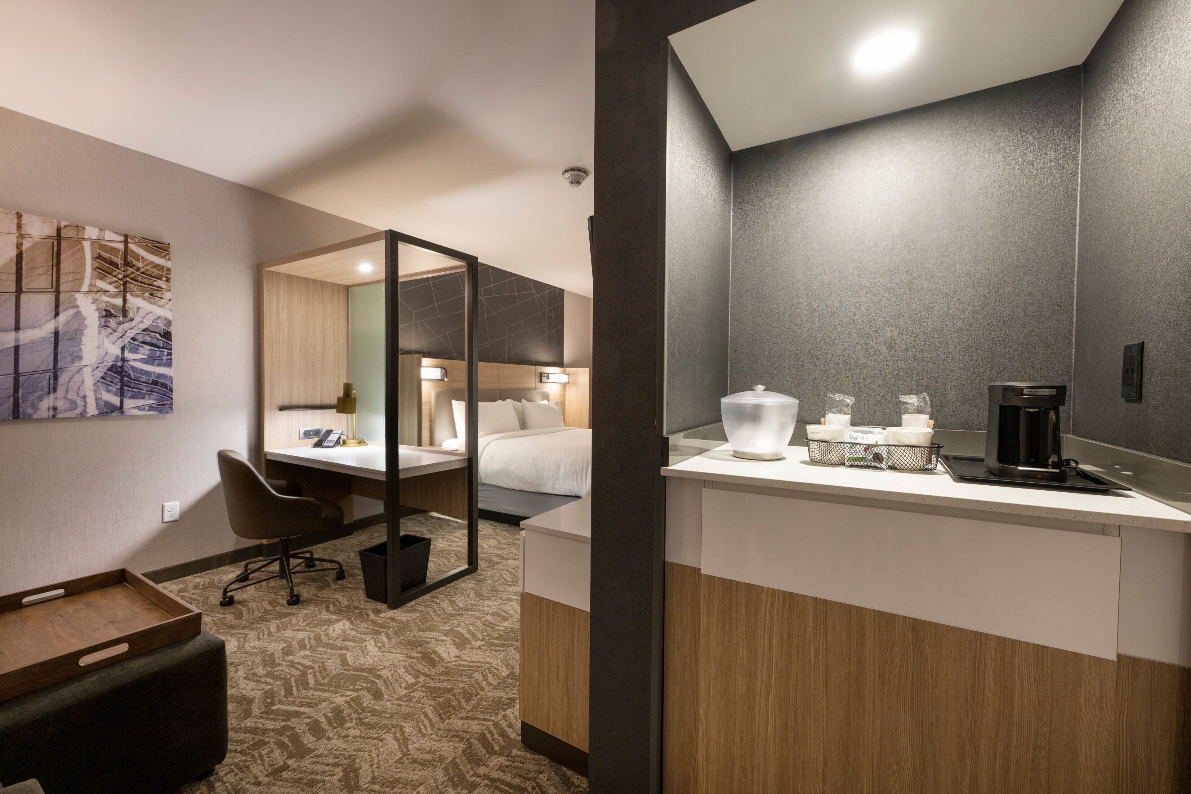 Een hotelkamer met een bed, bureau, stoel en een kleine kitchenette.