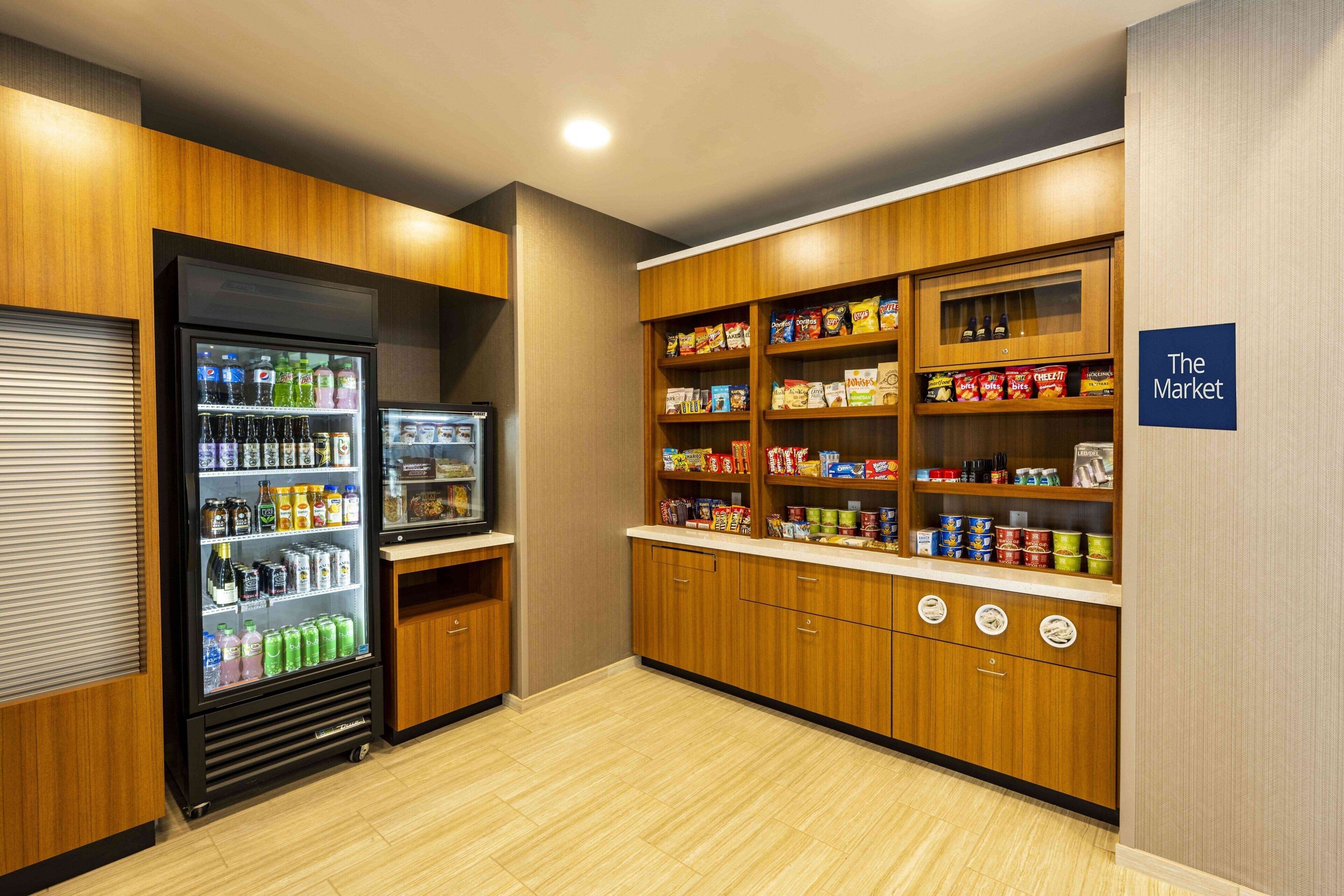 A kitchenette with a refrigerator stocked with beverages, a pantry with snacks, and a sign indicating 'The Market'.