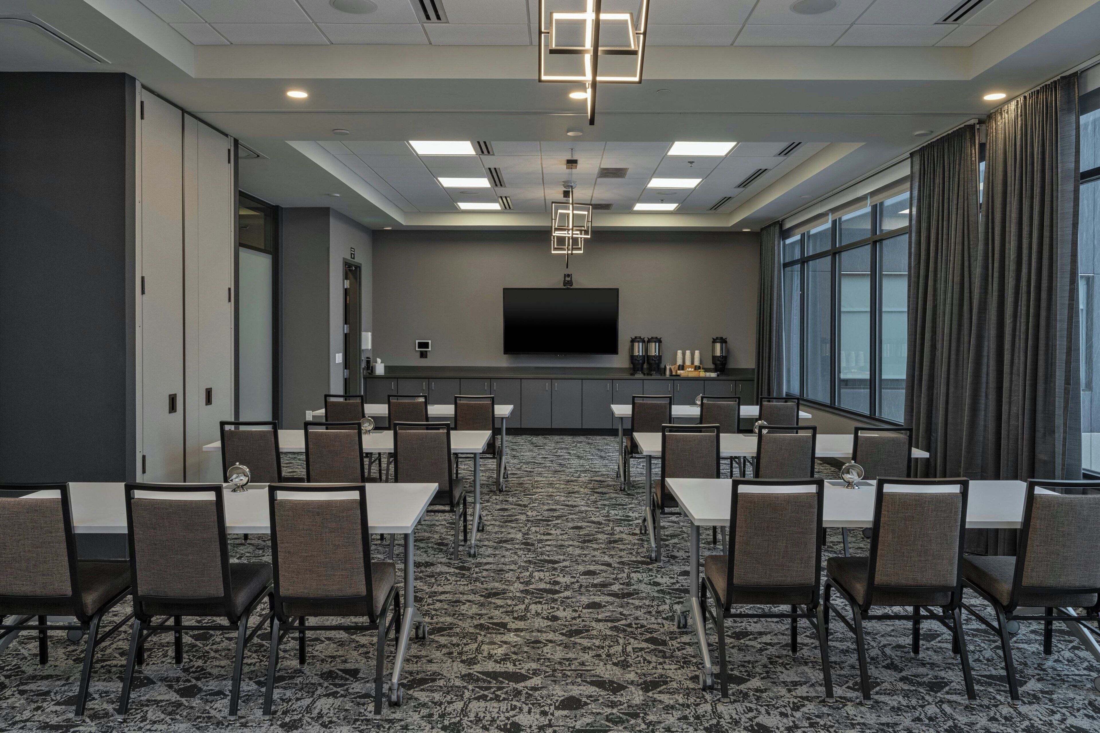 A conference room with tables and chairs, a flat-screen TV, and a large window with curtains.