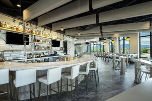 A modern bar area with a long counter, white bar stools, and a variety of bottles and glasses.