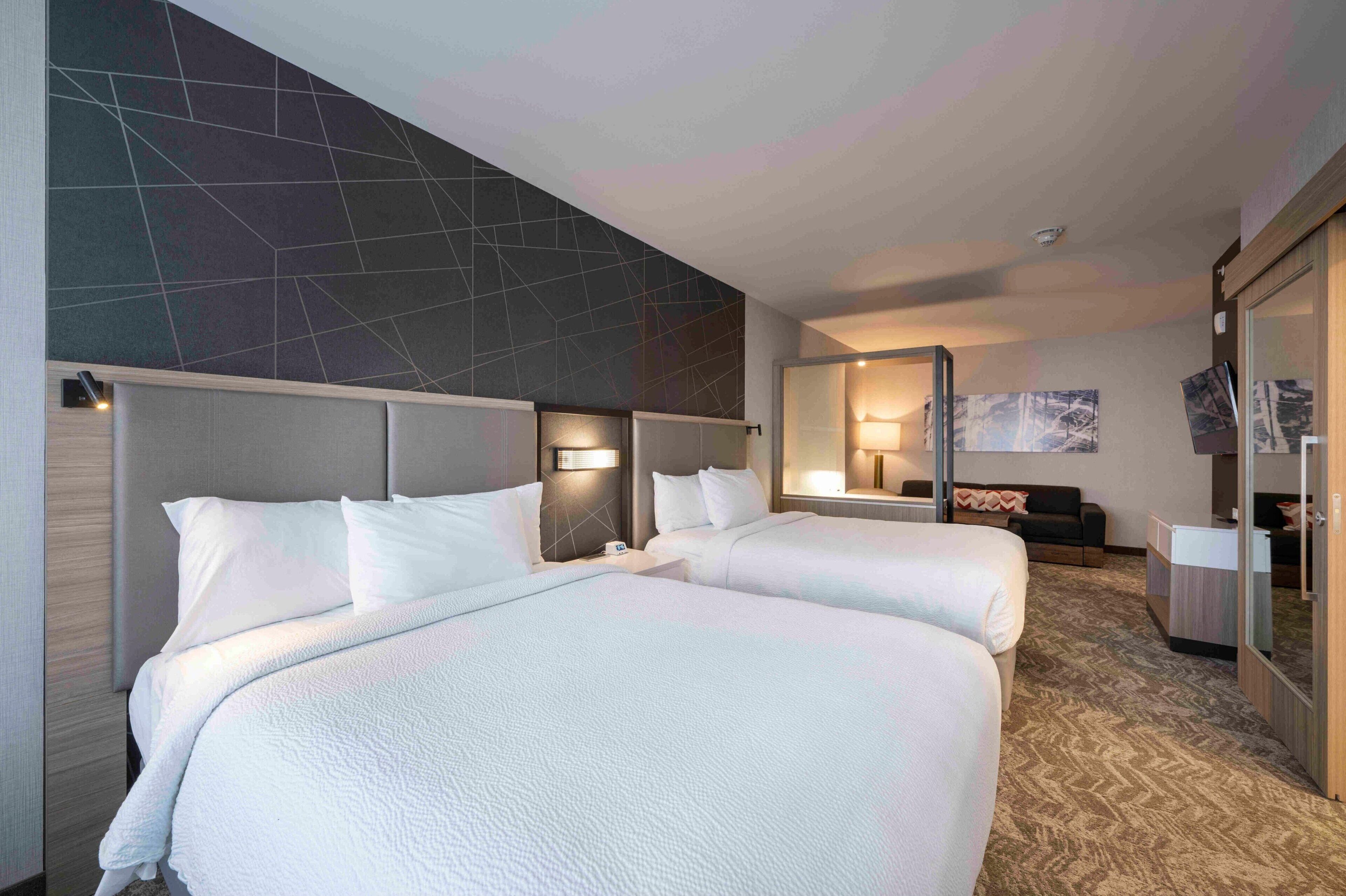 Ein Hotelzimmer mit zwei Betten, einem großen Spiegel und einem modernen Wanddesign mit geometrischen Formen.