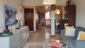 Een woonkamer met een bank, een bijzettafeltje en een eethoek op de achtergrond.
