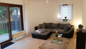 A living room with a sectional sofa, a glass coffee table, and a sliding glass door leading to a patio. - Ground floor apartment with large balcony. Terrace near the forest, to feel good (Schöneck)