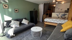 A compact living space with a grey sofa, a small round table, and a bed with a patterned bedspread. - Studio Buron des Gardes (Le Lioran)