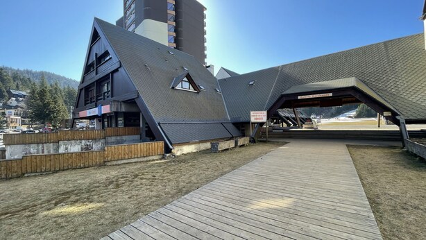 A modern building with a sloped roof and a wooden deck in front. - Studio Buron des Gardes (Le Lioran)