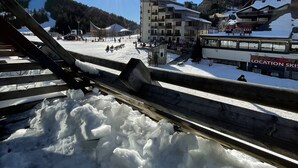 A snowy ski resort with a sunlit sky, a ski lift, and buildings with signage for a bar, restaurant, and pizzeria. - Studio Buron des Gardes (Le Lioran)