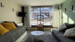 A modern living room with a grey sofa, a round coffee table, and a view of a snowy mountain through a large window. - Studio Buron des Gardes (Le Lioran)