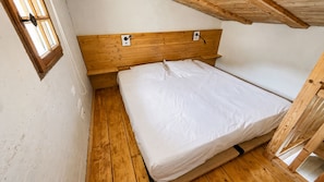 Ein kleines Zimmer mit einem Einzelbett, einem Holz-Kopfteil, Holzboden und einem Fenster mit Holzrahmen.