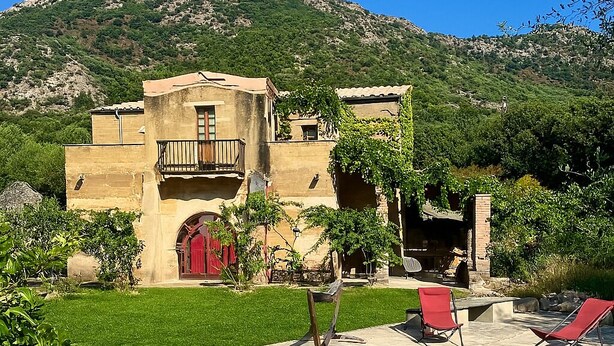A pool area with a clear blue pool, surrounded by a well-maintained lawn, and a building with a red door in the background. - L'Ombria – Charming Villa with a Private Pool (Belgodère)