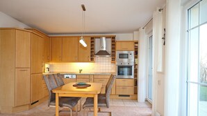 Eine moderne Küche mit Holzschränken, einem Esstisch mit Stühlen und einem großen Fenster, das für natürliches Licht sorgt.