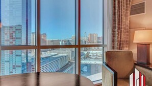 A modern hotel room with large windows offering a city view, a round table, a chair, and a lamp. - MGM Signature-Jacuzzi F1 Track & Strip View Studio (Las Vegas)