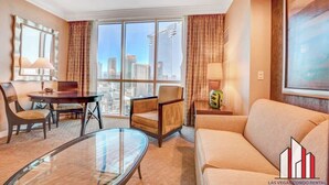 A modern hotel room with a glass coffee table, a sofa, a chair, and a dining table. There is a large window with a city view. - MGM Signature-Jacuzzi F1 Track & Strip View Studio (Las Vegas)