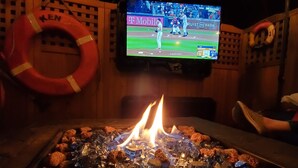 Une pièce avec un téléviseur diffusant un match de baseball, un foyer avec des braises incandescentes et un gilet de sauvetage accroché au mur.