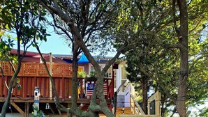 Une porte en bois, agrémentée d’une pancarte « Bienvenue » et d’une autre indiquant « Parking réservé aux invités », mène à un bâtiment doté d’un toit rouge et d’une marquise bleue.