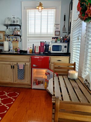 A kitchen with a red refrigerator, a microwave, and a coffee maker. There is a window with blinds and a hanging light fixture.