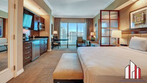 A hotel room with a bed, a desk, a chair, a TV, and a view of the city. - MGM Signature-29-607 F1 Track & Strip View Balcony (Las Vegas)