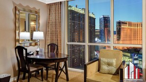 A hotel room with a large window offering a city view, a dining table with chairs, a sofa, and a mirror with a lamp. - MGM Signature-29-607 F1 Track & Strip View Balcony (Las Vegas)