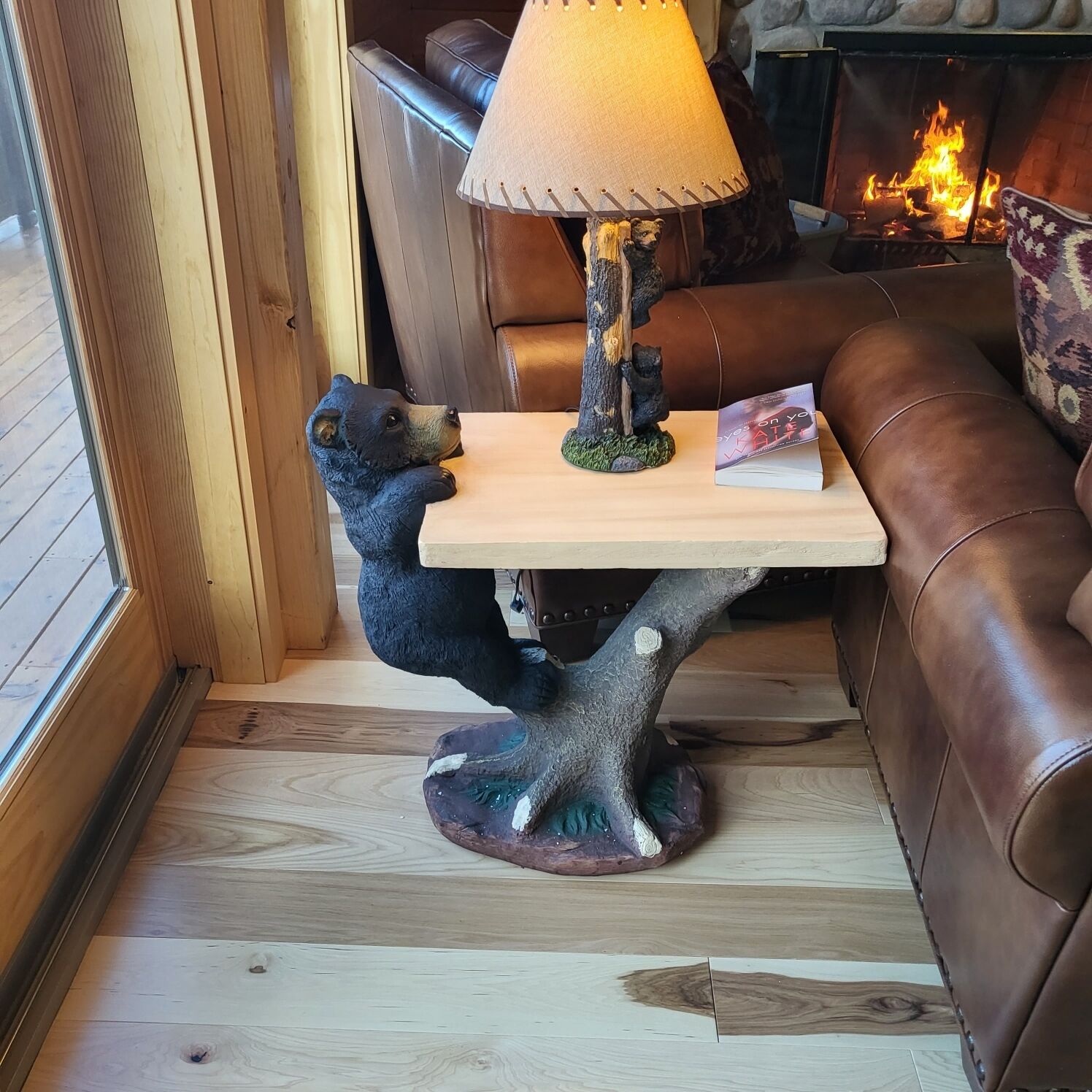 A wooden table with a bear sculpture, a lamp, and a book.