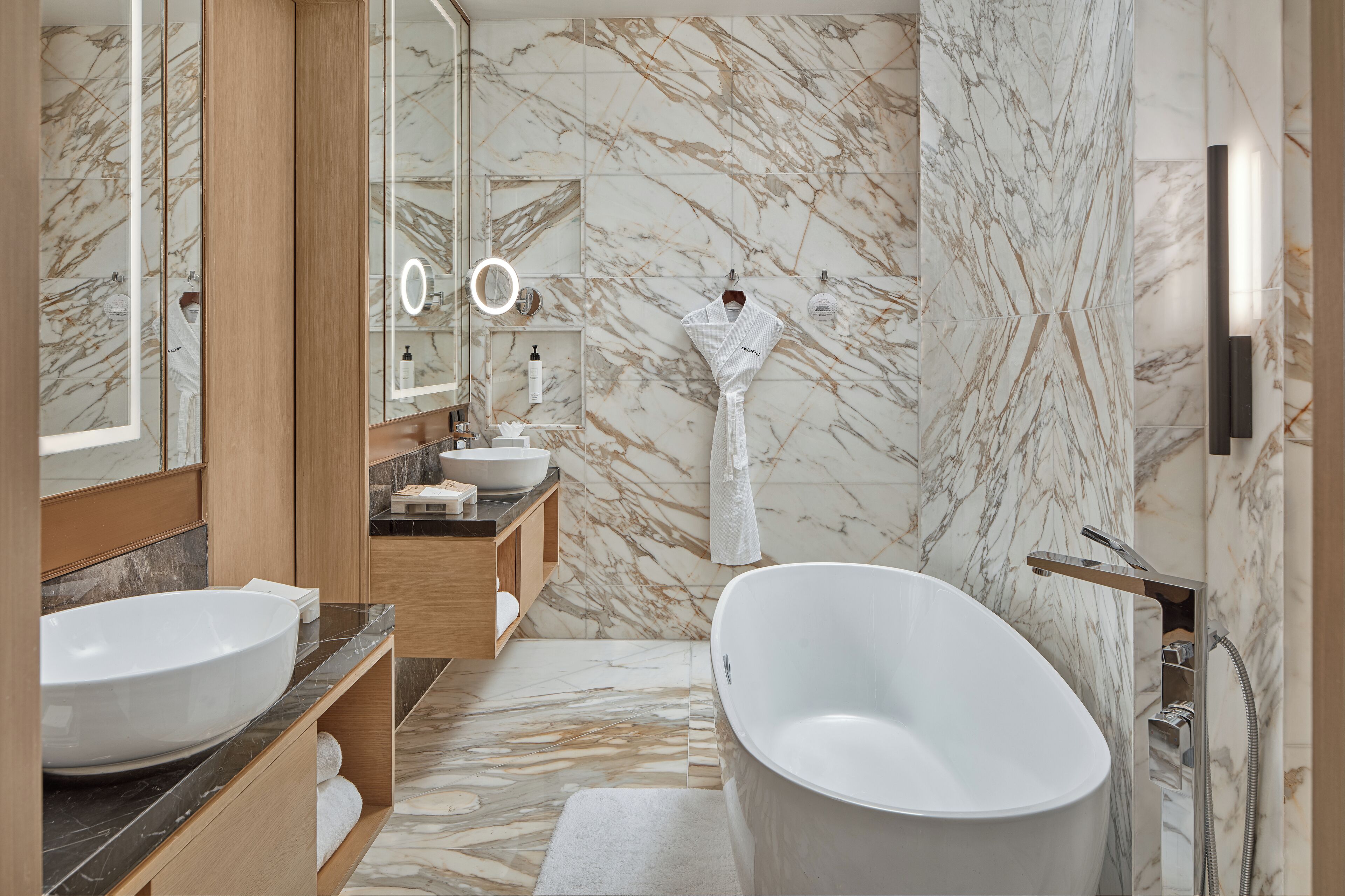 Un baño moderno con una bañera independiente grande, un tocador doble y paredes de mármol.