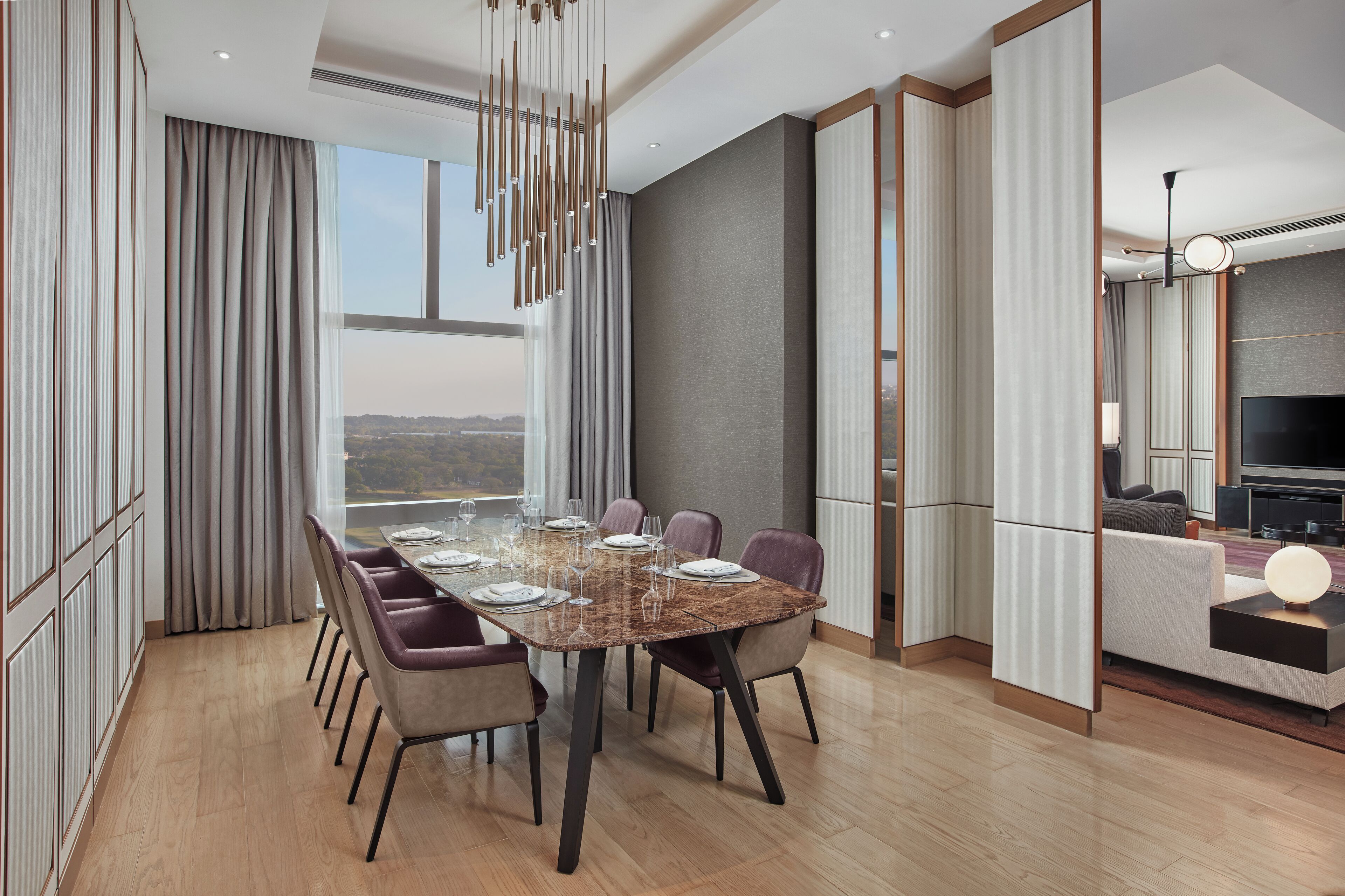 Un comedor moderno con una mesa grande dispuesta para seis personas, rodeada de sillas, en una habitación con ventanas amplias y vista a la ciudad.