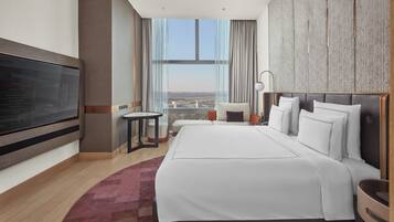 A modern hotel room with a large bed, a flat-screen TV, a small table, and a view of the city.