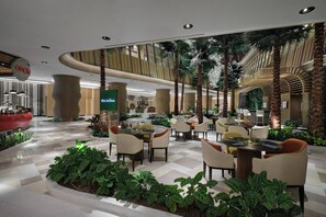 Un espacio interior amplio con diversas disposiciones de asientos, una columna decorativa central y una variedad de plantas.