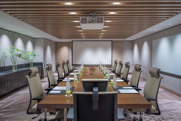 A conference room with a long table, chairs, a projector, and a screen.