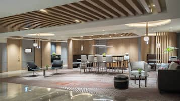 Un moderno vestíbulo de hotel con un área de estar central, un mostrador de recepción y un comedor.