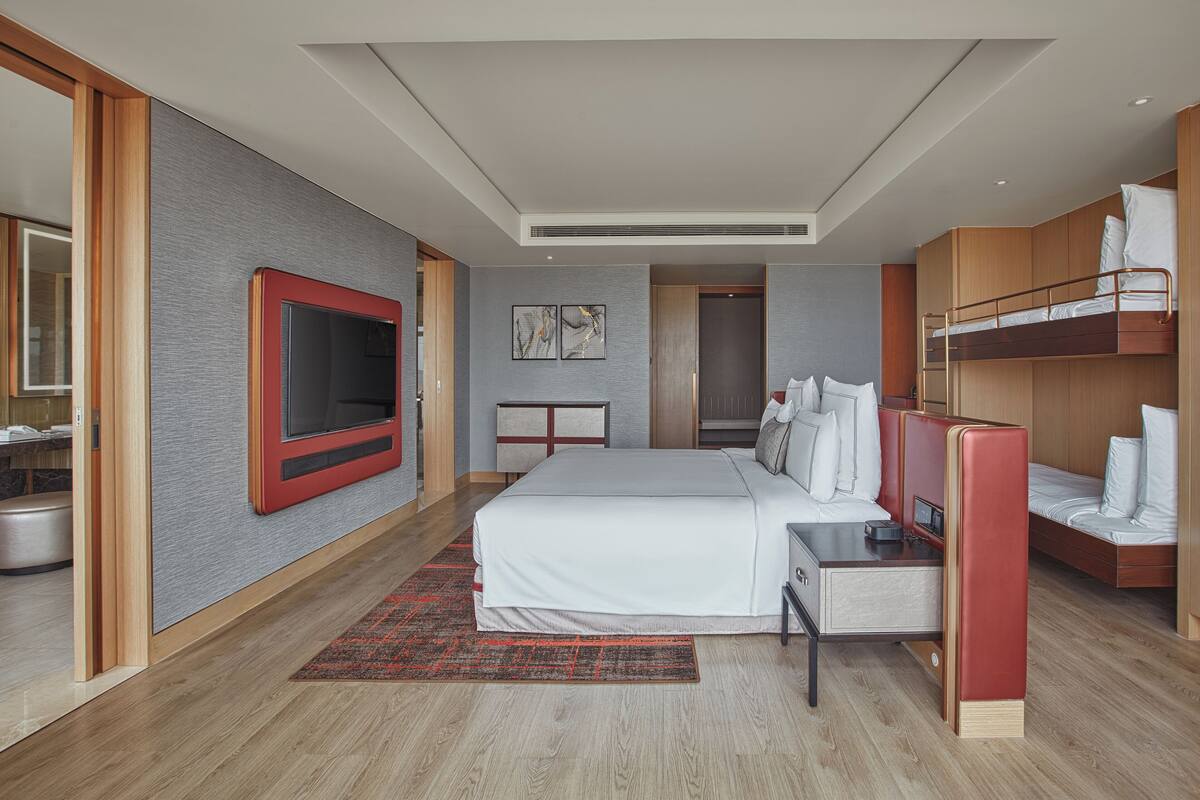 A modern hotel room with a large bed, a TV, a desk, and a bunk bed.