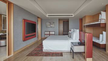 A modern hotel room with a large bed, a TV, a desk, and a bunk bed.