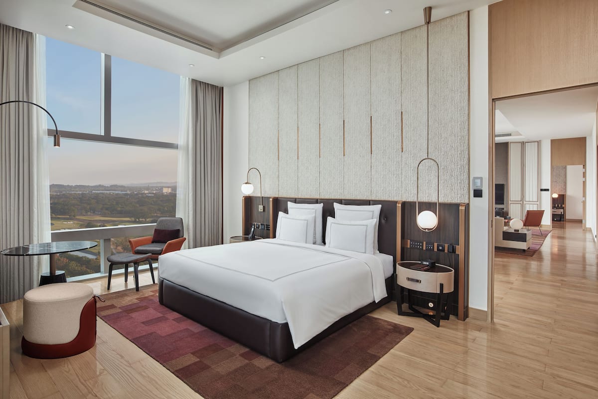 A modern hotel room with a large bed, a desk, a chair, and a view of the cityscape.