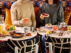 Une table à manger, sur laquelle sont disposés divers plats et boissons, entourée de chaises dont les revêtements sont ornés de motifs.