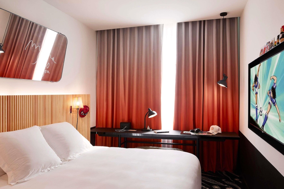 Una habitación de hotel con cama, escritorio con lámpara, televisor y cortinas.