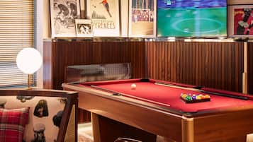 Une table de billard avec des billes, un téléviseur diffusant un événement sportif et, au mur, des objets de collection encadrés liés au sport.