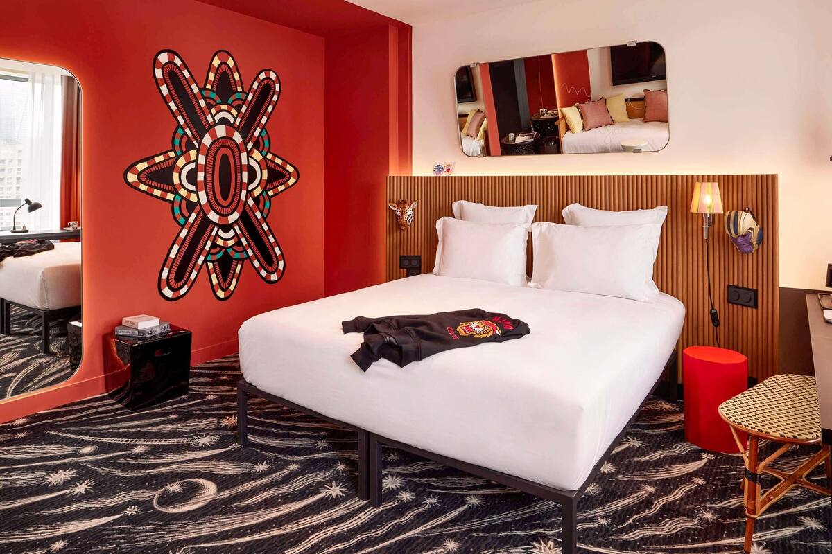 A hotel room with a large bed, a mirror, a wall art piece, and a red accent wall.