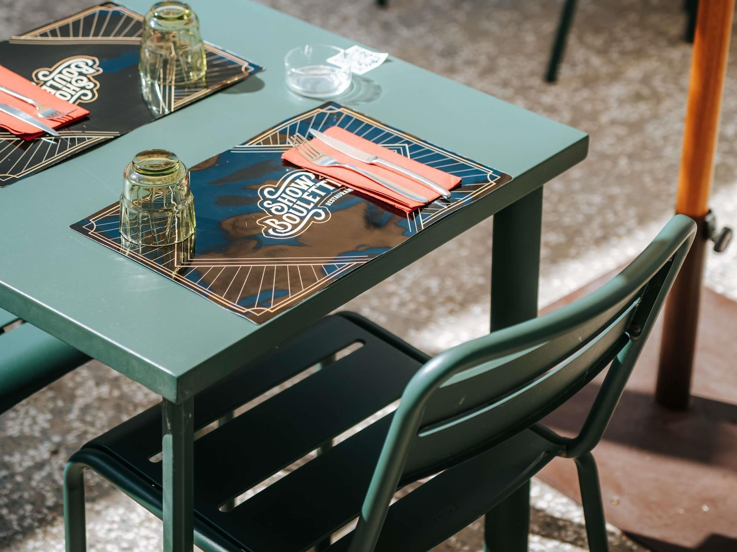 A table with a black placemat featuring a logo, a glass with a drink, and a folded orange napkin.