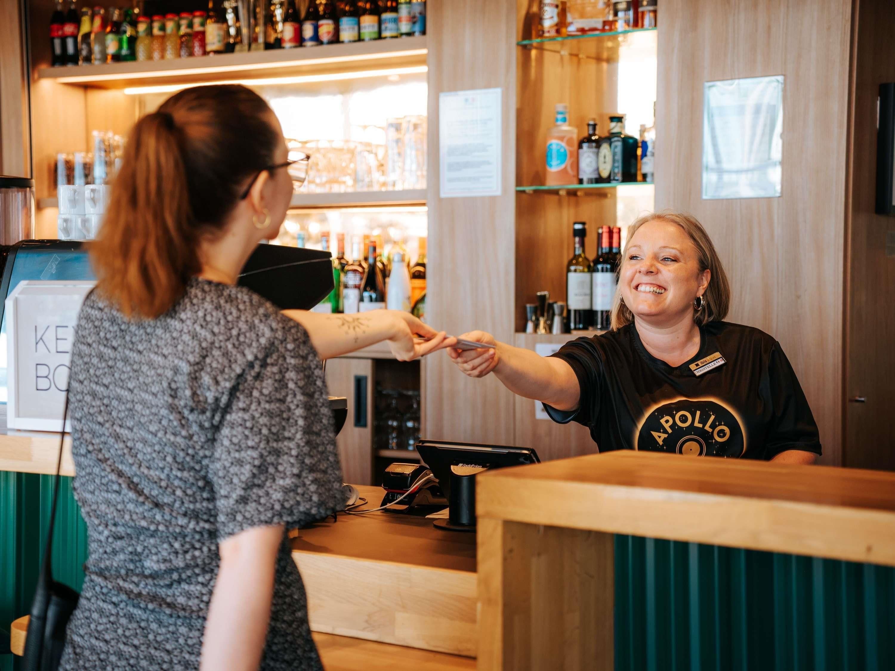 A bar area with a counter, a cash register, and shelves stocked with bottles.