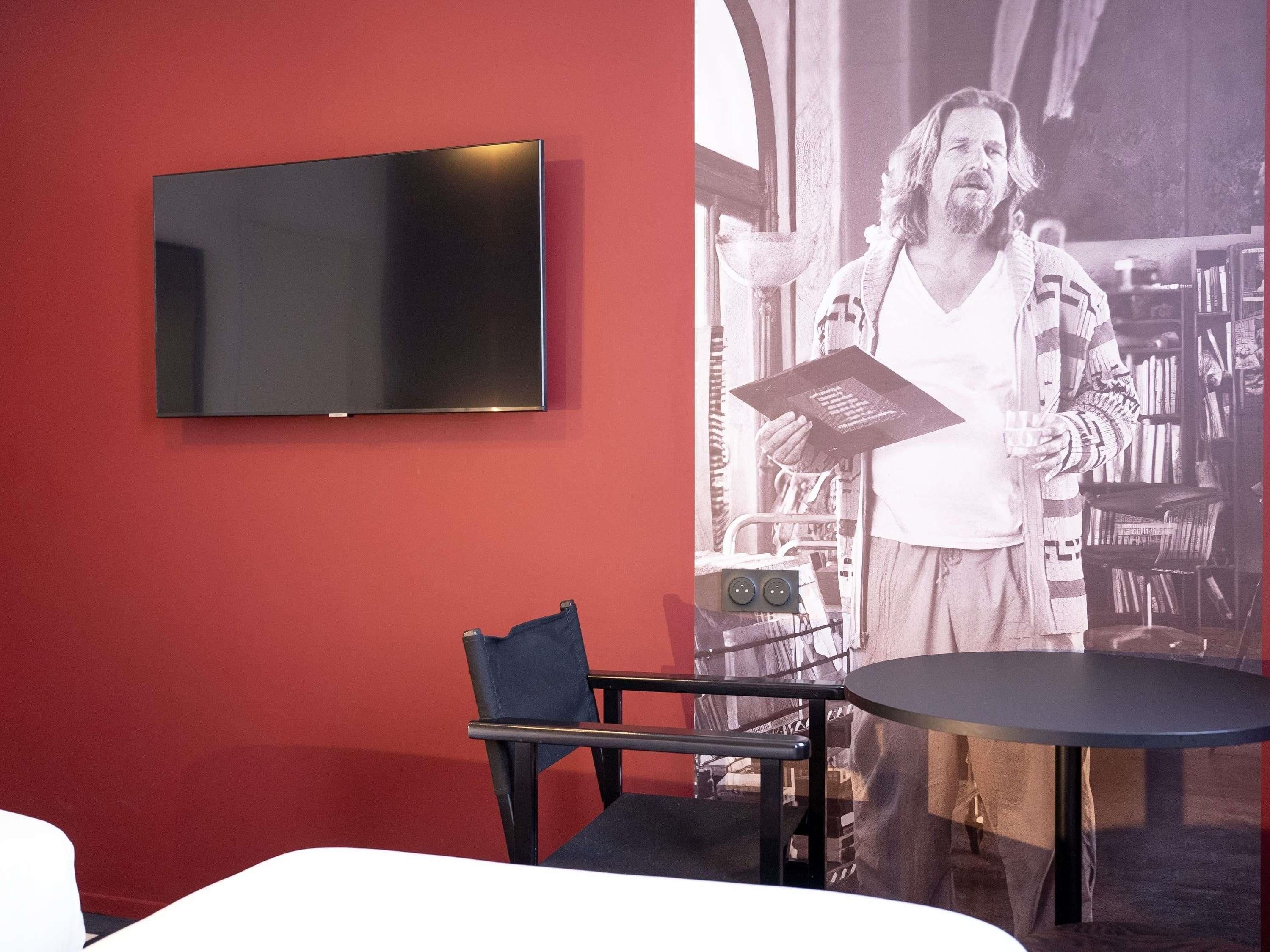 A room with a flat-screen TV mounted on a red wall, a black chair with a cushion, and a round table.