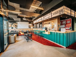 A bar area with seating, a bar counter, and a screen displaying movie titles. - Ibis Styles Lens Centre Gare (Lens)